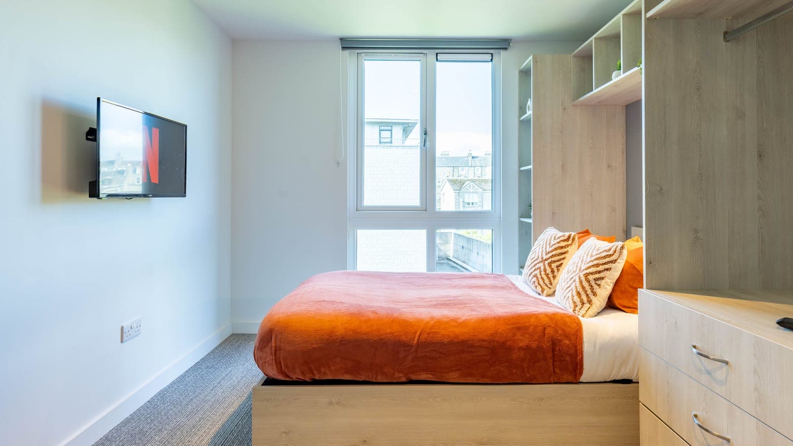 A made bed beside the window in an en-suite room at ABeleven, with a wall-mounted television